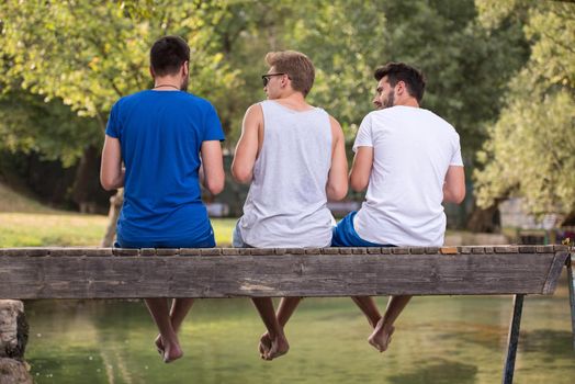 group of young men enjoying watermelon while sitting on the wooden bridge over the river in beautiful nature