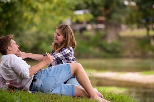 Couple in love enjoying picnic time drink and food in beautiful nature on the river bank