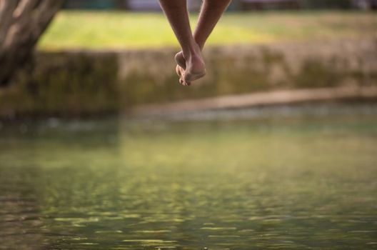 group of  people sitting at wooden bridge over the river with a focus on hanging legs