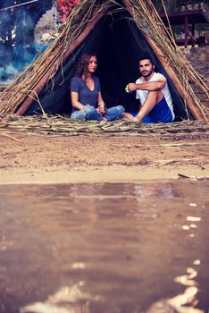 couple in love traveling and spending time together in straw tent while drinking hot tea by the river