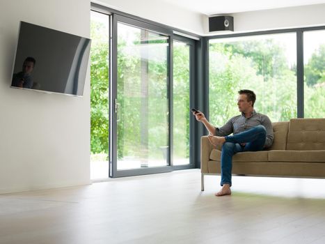 young handsome man enjoying free time watching television in his luxury home villa