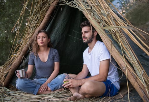 couple in love traveling and spending time together in straw tent while drinking hot tea by the river