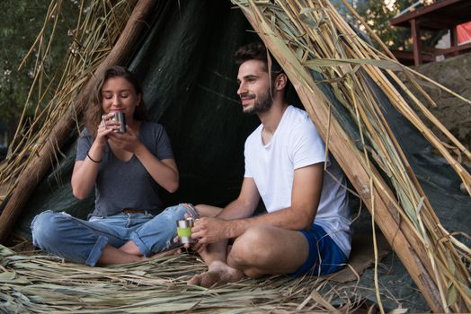 couple in love traveling and spending time together in straw tent while drinking hot tea by the river