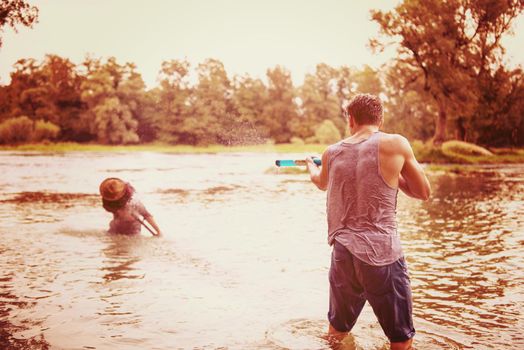 young men having fun with water guns while splashing  each other during sunset on the river