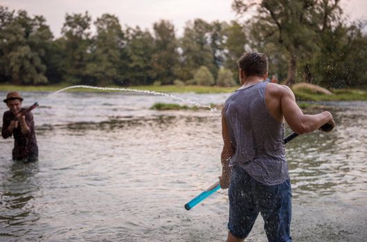 young men having fun with water guns while splashing  each other during sunset on the river