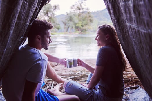 couple in love traveling and spending time together in straw tent while drinking hot tea by the river