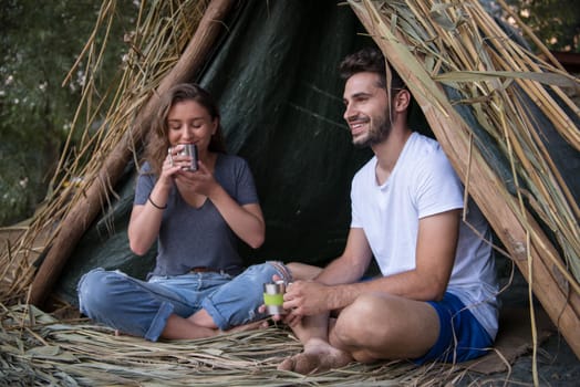 couple in love traveling and spending time together in straw tent while drinking hot tea by the river