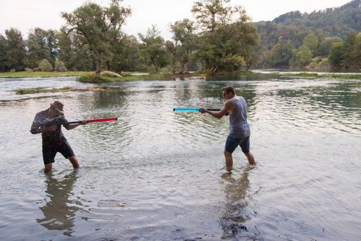 young men having fun with water guns while splashing  each other during sunset on the river