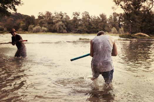 young men having fun with water guns while splashing  each other during sunset on the river