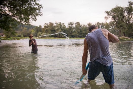 young men having fun with water guns while splashing  each other during sunset on the river