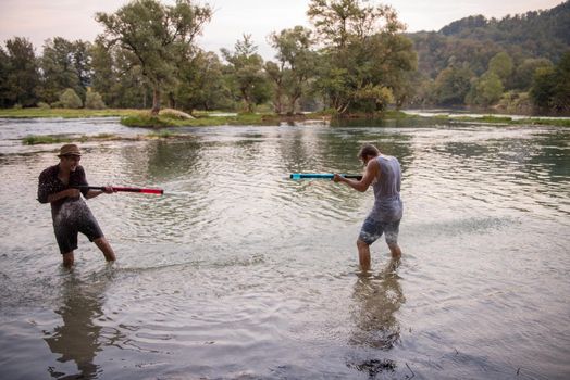 young men having fun with water guns while splashing  each other during sunset on the river