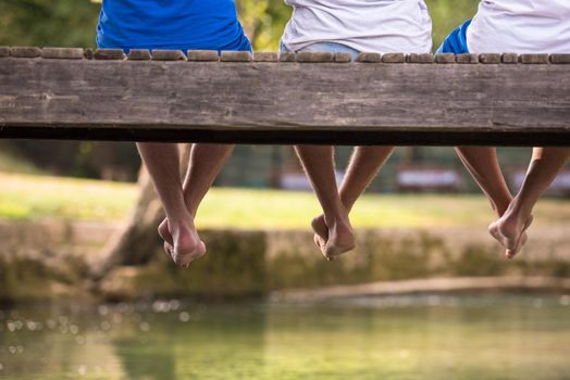 group of  people sitting at wooden bridge over the river with a focus on hanging legs