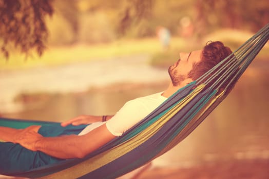 Young man resting on hammock while enjoying nature on the river bank