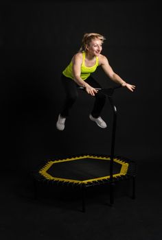 Girl on a fitness trampoline on a black background in a yellow t-shirt trampoline jump, activity muscular rebounder. white physical muscle instructor enjoy