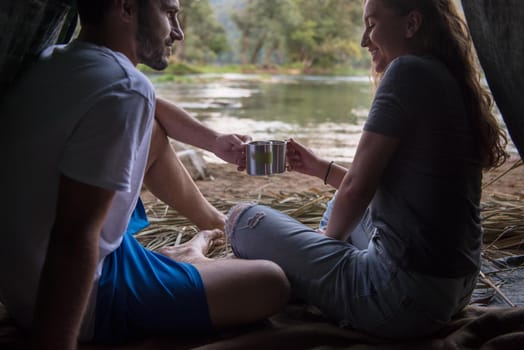 couple in love traveling and spending time together in straw tent while drinking hot tea by the river