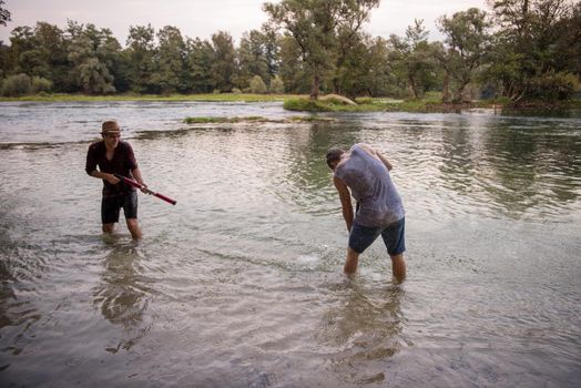 young men having fun with water guns while splashing  each other during sunset on the river