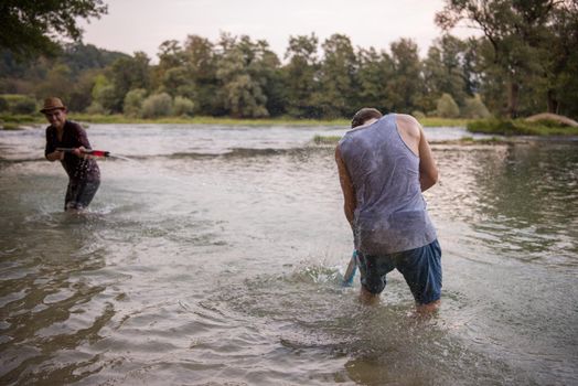 young men having fun with water guns while splashing  each other during sunset on the river