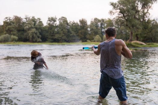 young men having fun with water guns while splashing  each other during sunset on the river