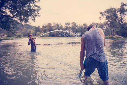 young men having fun with water guns while splashing  each other during sunset on the river