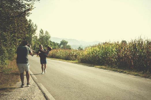 young videographer with gimball video slr rocording while man carries a woman in his arms during jogging along a country road, exercise and fitness concept