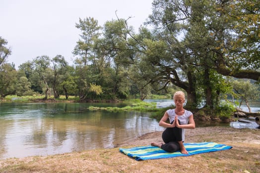 healthy woman relaxing while meditating and doing yoga exercise in the beautiful nature on the bank of the river