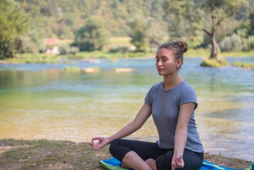 healthy woman relaxing while meditating and doing yoga exercise in the beautiful nature on the bank of the river