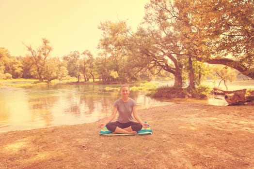 healthy woman relaxing while meditating and doing yoga exercise in the beautiful nature on the bank of the river