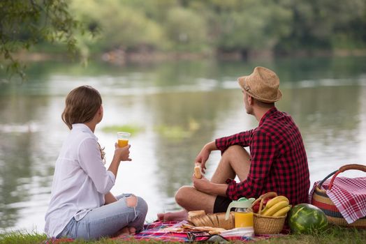 Couple in love enjoying picnic time drink and food in beautiful nature on the river bank