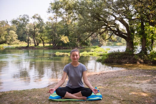 healthy woman relaxing while meditating and doing yoga exercise in the beautiful nature on the bank of the river