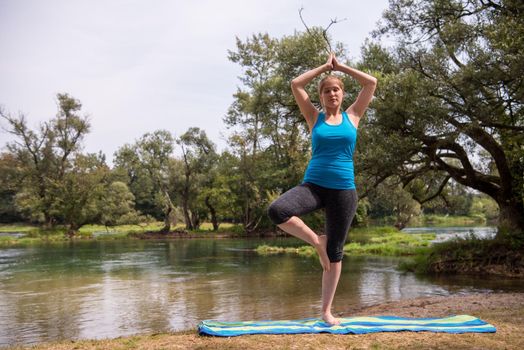 healthy woman relaxing while meditating and doing yoga exercise in the beautiful nature on the bank of the river