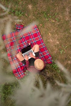 A young freelancer using a laptop computer while working in beautiful nature under the tree top view