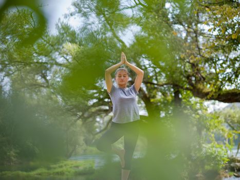 healthy woman relaxing while meditating and doing yoga exercise in the beautiful nature on the bank of the river