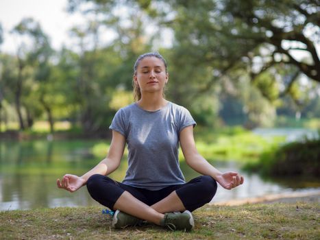 healthy woman relaxing while meditating and doing yoga exercise in the beautiful nature on the bank of the river