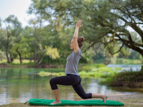 healthy woman relaxing while meditating and doing yoga exercise in the beautiful nature on the bank of the river