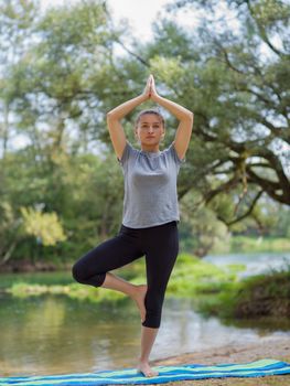 healthy woman relaxing while meditating and doing yoga exercise in the beautiful nature on the bank of the river