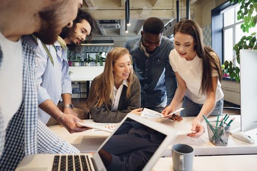 Team of diverse multiracial coworkers in modern office discuss their project together