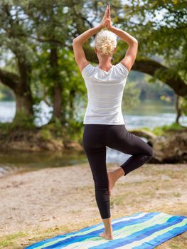 healthy woman relaxing while meditating and doing yoga exercise in the beautiful nature on the bank of the river