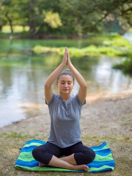 healthy woman relaxing while meditating and doing yoga exercise in the beautiful nature on the bank of the river