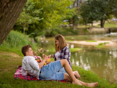 Couple in love enjoying picnic time drink and food in beautiful nature on the river bank