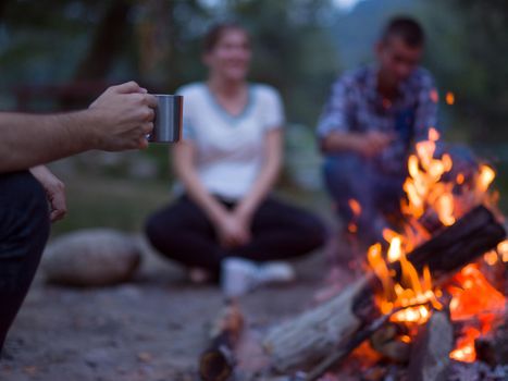 a group of happy young friends relaxing and enjoying  summer evening around campfire on the river bank