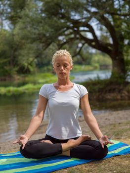 healthy woman relaxing while meditating and doing yoga exercise in the beautiful nature on the bank of the river