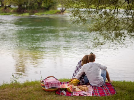 Couple in love taking a selfie by mobile phone while enjoying picnic time drink and food in beautiful nature on the river bank