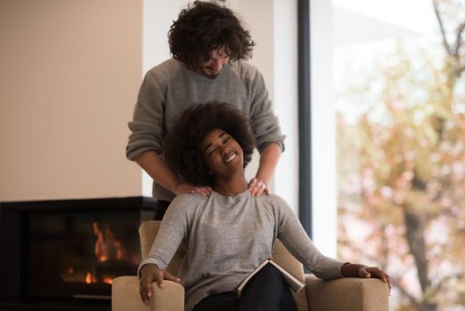 Young beautiful multiethnic couple hugging in front of fireplace at home when reading a book at autumn day