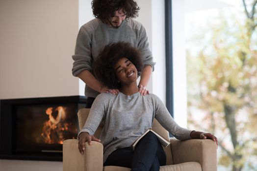 Young beautiful multiethnic couple hugging in front of fireplace at home when reading a book at autumn day