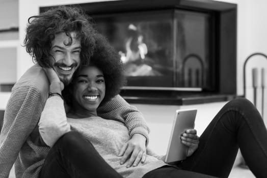 beautiful young multiethnic couple used tablet computer on the floor of their luxury home in front of fireplace autumn day