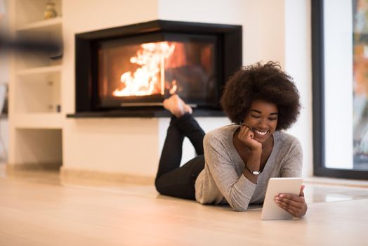 beautiful young black women using tablet computer on the floor of her luxury home in front of fireplace at autumn day