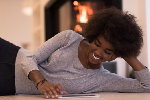 beautiful young black women using tablet computer on the floor of her luxury home in front of fireplace at autumn day