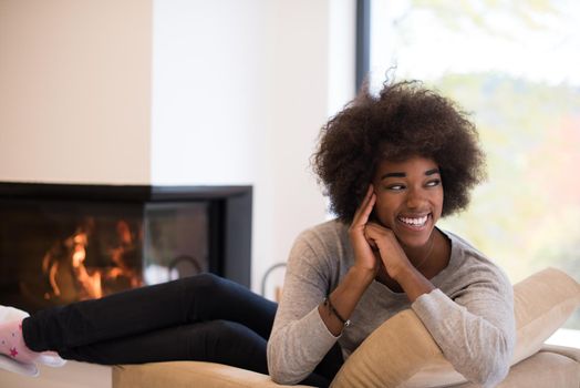 Young beautiful african american woman relaxing on chair in front of fireplace at autumn day