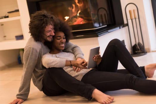 beautiful young multiethnic couple using tablet computer on the floor of their luxury home in front of fireplace at autumn day