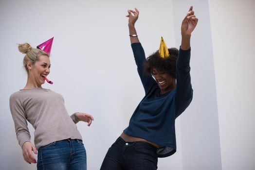 people and celebration concept  young multiethnics smiling women in party caps blowing to whistles